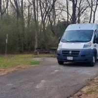 A white Promaster camper van is parked in a campsite at a campground.