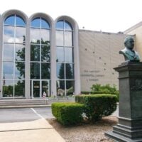 Building with bust on a pillar located outside by shrubs
