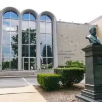 Building with bust on a pillar located outside by shrubs